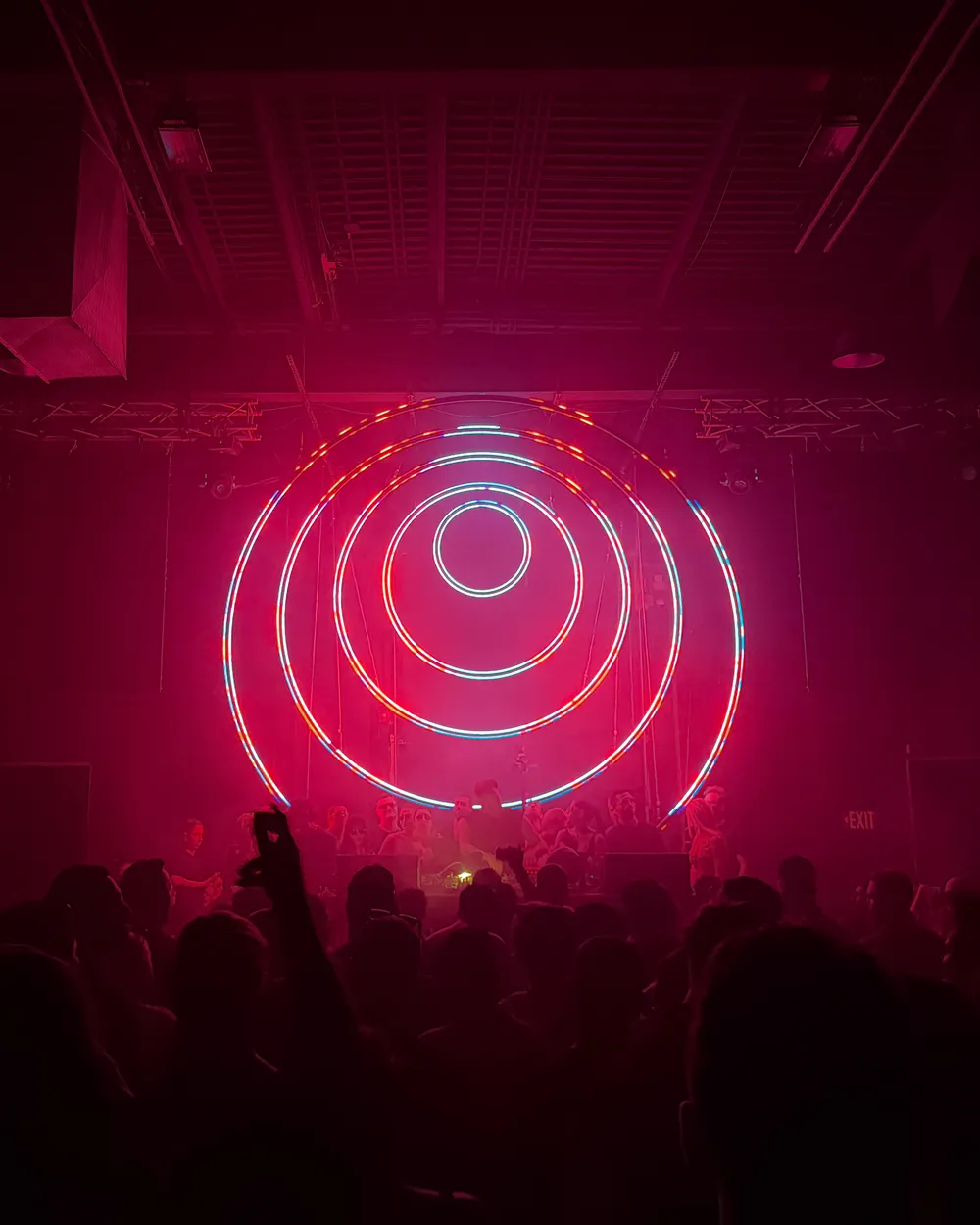 A crowd facing the stage under red concentric LED rings at Demo Room